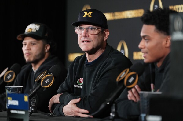 Michigan head coach Jim Harbaugh, center, with running back Blake Corum, left, and defensive back Will Johnson, right, speaks during an NCAA college football news conference Tuesday, Jan. 9, 2024, in Houston. Harbaugh and No. 1 Michigan completed a three-year climb to a national championship by beating No. 2 Washington 34-13 Monday night in the College Football Playoff title game.(AP Photo/Eric Gay)