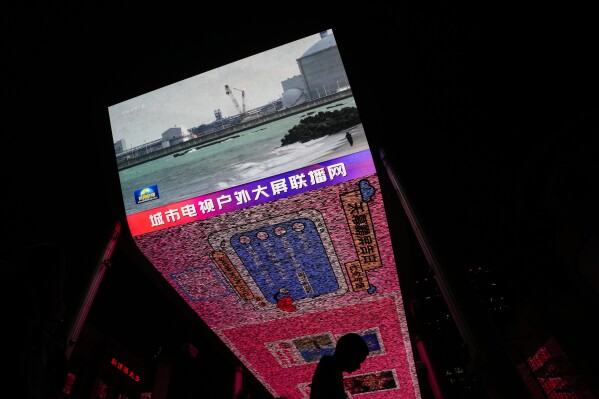A man walks by a large screen at a shopping mall showing CCTV broadcasting news of Fukushima Daiichi nuclear power plant began releasing its first batch of treated radioactive water into the Pacific Ocean, in Beijing, Thursday, Aug. 24, 2023. (AP Photo/Andy Wong)
