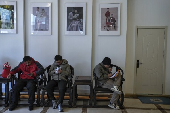 Chinese job seekers browse their smartphones against a wall displaying wedding and family photographs, as they look for job vacancies at a job fair in Beijing on Feb. 23, 2024. China's efforts to restore confidence and rev up the economy will top the agenda during this month’s meeting of the ceremonial national legislature. (AP Photo/Andy Wong)