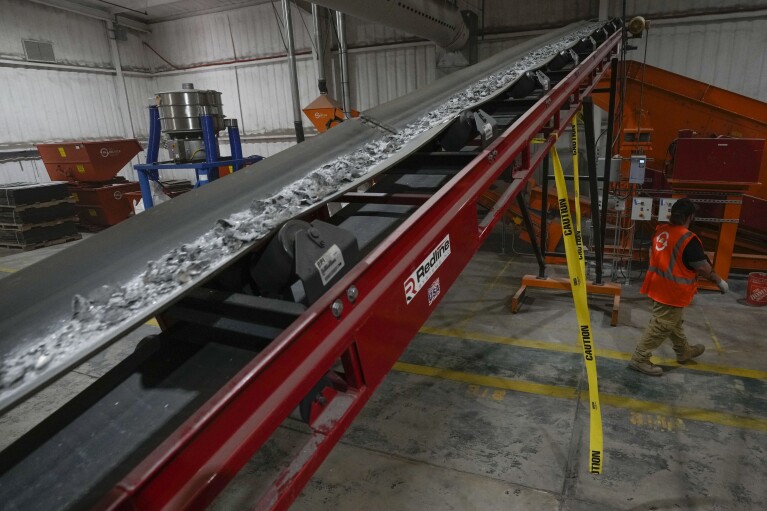K.C. Skilern walks under a sorting machine as solar panels are broken down and processed at We Recycle Solar on Tuesday, June 6, 2023, in Yuma, Ariz. (AP Photo/Gregory Bull)