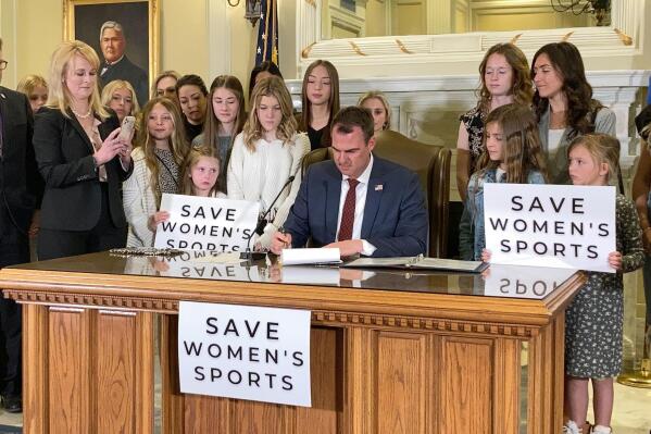 Oklahoma Gov. Kevin Stitt signs a bill in Oklahoma City on Wednesday, March 30, 2022, that prevents transgender girls and women from competing on female sports teams. Stitt signed the bill flanked by more than a dozen young female athletes, including his eighth-grade daughter Piper. (AP Photo/Sean Murphy)