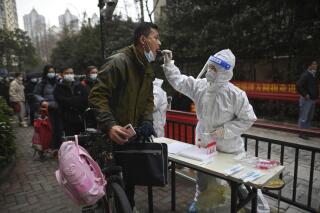 A man holding his bicycle with a school bag on it gets a throat swab during a mass COVID-19 test at a residential compound in Wuhan in central China's Hubei province, Tuesday, Feb. 22, 2022. Wuhan, the first major outbreak of the coronavirus pandemic has reported more than dozen new coronavirus cases this week, prompting the authority to step up precautious measures. (Chinatopix via AP)