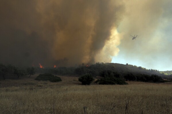 A helicopter flies over a wildfire near Vatontas village on the Aegean Sea island of Evia, Greece, Monday, Aug. 21, 2023. Major wildfires were burning in Greece and on one of Spain's Canary Islands off the African coast Monday, with hot, dry and windy conditions hampering the efforts of hundreds of firefighters battling the blazes, two of which have been burning for several days. (AP Photo/Thodoris Nikolaou)