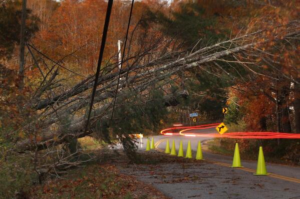 FILE - A car leaves a trail of light as it passes under power lines weighed down by toppled trees in Freeport, Maine, Tuesday, Oct. 31, 2017. Weather disasters fueled by climate change now roll across the U.S. year-round, battering the nation's aging electric grid. (AP Photo/Robert F. Bukaty, File)