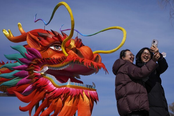 Women take a selfie with a giant dragon lantern decorated near the frozen Houhai Lake in Beijing, Thursday, Feb. 8, 2024. (AP Photo/Andy Wong)