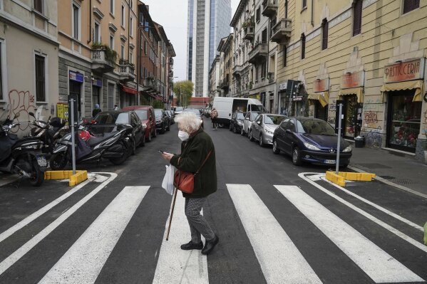 An elderly woman crosses a street in Milan, Italy, Tuesday, Dec. 1, 2020. In Italy, which has the world's second-oldest population, many people in their 70s and older have kept working through the COVID-19 pandemic. From neighborhood newsstand dealers to farmers bring crops to market, they are defying stereotypic labels that depict the old as a monolithic category that's fragile and in need of protection.  (AP Photo/Luca Bruno)