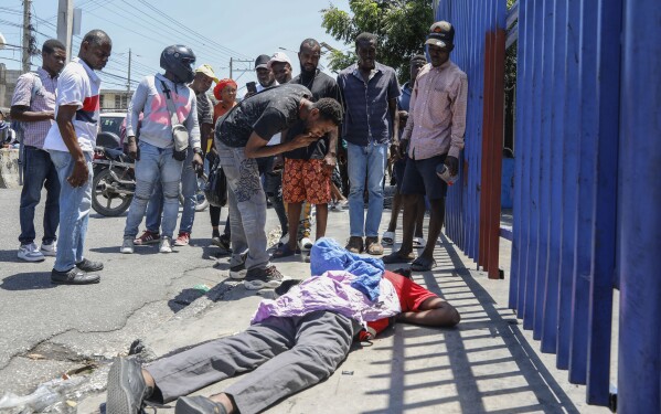 People observe the body of a man lying on the street of the Delmas 30 neighborhood in Port-au-Prince, Haiti, Monday, April 1, 2024. Witnesses reported that he was struck by a stray bullet during a shootout between police and gangs. (AP Photo/Odelyn Joseph)