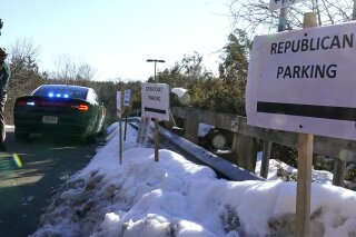 FILE - In this Feb. 24, 2021, file photo, a sign directs Republican and Democrat legislators to their parking areas as a N.H. State Trooper watches the flow of traffic prior to a New Hampshire House of Representatives session held at NH Sportsplex, due to the coronavirus in Bedford, N.H. Amid calls to dial back hyper political partisanship, two letters are among the obstacles standing in the way. Republicans, including the lawyers who defended former President Donald Trump during last week’s impeachment trial, routinely drop the “i-c” when referring to the Democratic Party or its policies. (AP Photo/Charles Krupa, File)