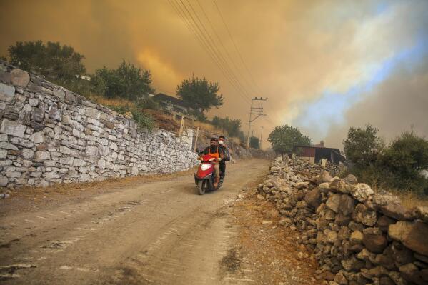 People drive away from an advancing fire in Cokertme village, in Bodrum, Mugla, Turkey, Monday, Aug. 2, 2021. For the sixth straight day, Turkish firefighters were battling Monday to control the blazes tearing through forests near Turkey's beach destinations. Fed by strong winds and scorching temperatures, the fires that began Wednesday have left eight people dead and forced residents and tourists to flee vacation resorts in a flotilla of small boats.(AP Photo/Emre Tazegul)