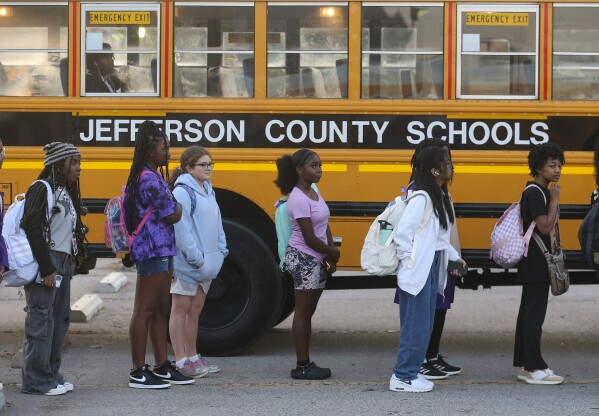 Jefferson County Public School students stand beside their bus as they prepare to transfer buses on Friday, Aug. 18, 2023 in Louisville, Ky. . Jefferson County Schools, a public district with more than 90,000 students, drew up new bus routes and staggered school start times under a new plan that officials hoped would alleviate issues caused by driver shortages. (Michael Clevenger/Courier Journal via AP)