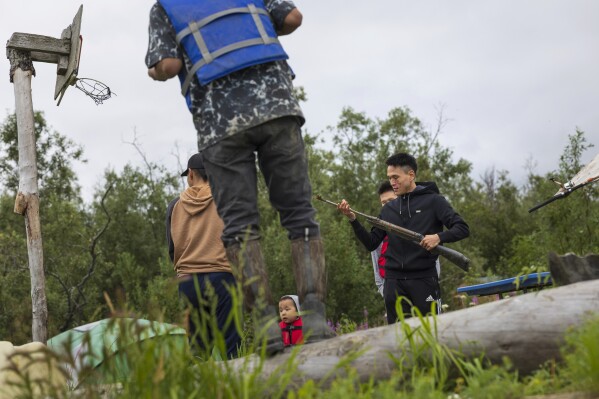 Tyson Ivanoff Sample examines a rusted pellet rifle inside a fish camp on the Kuskowim River, Saturday, Aug. 19, 2023, in Akiachak, Alaska. Fishing camps occupied by villagers serve as staging grounds to prepare fish and wildlife obtained along the waterfront. (AP Photo/Tom Brenner)