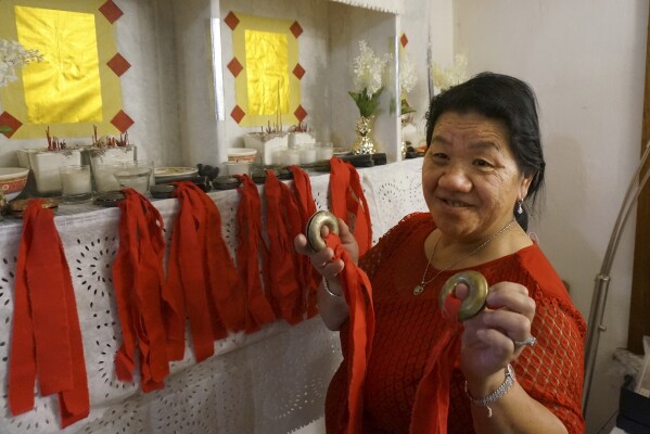 Mee Vang Yang holds her father's ring-shaped shaman bells in front of the altar in her living room in St. Paul, Minn., on Friday, Nov. 17, 2023. Vang Yang carried them across the Mekong River as the family fled the Communist takeover of her native Laos four decades ago. Today, they facilitate the connection to the spiritual world she needs to help fellow refugees and their American-raised children who seek restoration of lost spirits. (AP Photo/Giovanna Dell'Orto)
