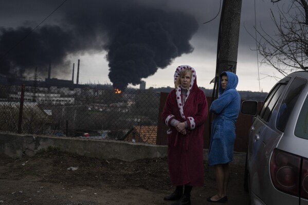Women stand next to a car as smoke rises in the air in the background after shelling in Odesa, Ukraine, Sunday, April 3, 2022. (AP Photo/Petros Giannakouris)