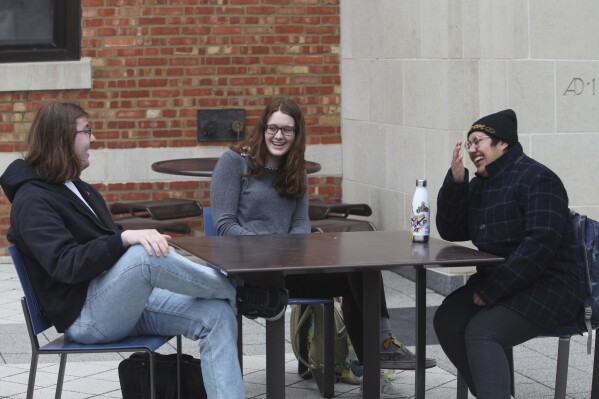 University of Kansas students, Chris Raithel, from left, Jenna Bellemere and Raine Flores-Peña, share a light moment outside the university's Memorial Union after an interview, Tuesday, Feb. 26, 2024, in Lawrence, Kan. The students are part of a push to get administrators to add transgender rights language to university policies. (AP Photo/John Hanna)