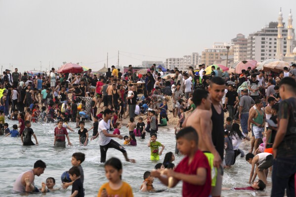FILE - People enjoy the day on the beach in the Mediterranean Sea during a heat wave in Gaza City, Friday, June 2, 2023. Gaza is tucked between Israel, Egypt and the Mediterranean Sea. The strip is 25 miles (40 kilometers) long by some 7 miles (11 kilometers) wide. It has a population of 2.3 million people living on an area of 139 square miles (360 square kilometers), according to the CIA Factbook. (AP Photo/Adel Hana, File)