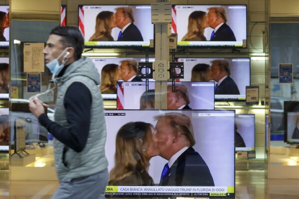 A man wearing a face mask walks by the window of a shop with TV screens showing an image of U.S. President Donald Trump during a news program, in Milan, Friday, Oct. 2, 2020. Trump said early Friday that he and first lady Melania Trump have tested positive for the coronavirus, a stunning announcement that plunges the country deeper into uncertainty just a month before the presidential election. (AP Photo/Luca Bruno)