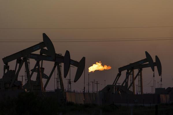 FILE - A flare burns off methane and other hydrocarbons as oil pumpjacks operate in the Permian Basin in Midland, Texas, Oct. 12, 2021. Two Texas companies have resolved Clean Air Act violations with the Environmental Protection Agency by agreeing to reduce emissions of planet-warming methane and other harmful pollutants wafting from the nation's largest oil and gas producing region. (AP Photo/David Goldman, File)
