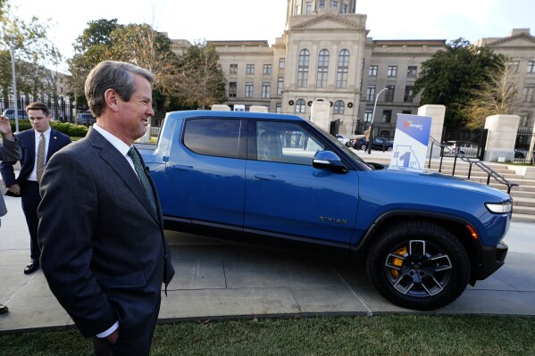 FILE - Gov. Brian Kemp smiles as he stands next to a Rivian electric truck during a ceremony to announce that the electric truck maker plans to build a $5 billion battery and assembly plant east of Atlanta projected to employ 7,500 workers, Thursday, Dec. 16, 2021, in Atlanta. Kemp is escalating his attack on President Joe Biden’s electric vehicle policy. The Republican governor spoke Tuesday, June 27, 2023 at the groundbreaking for a company that got more than $100 million in federal funding to refine graphite for electric batteries. But Kemp says Biden's infrastructure law wrongly puts the government's “thumb on the scale.” (AP Photo/John Bazemore, File)
